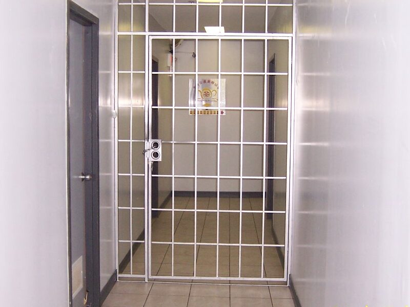 The image shows a hallway with a locked metal security gate restricting access. The presence of this barrier could pose a potential obstruction to the means of egress, which is crucial for safe evacuation during an emergency. Proper egress routes must remain unobstructed and accessible to comply with fire safety regulations. The image appears to highlight an inspection or assessment of compliance with building safety and fire codes.