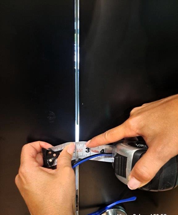 The image captures a close-up of a person measuring the gap between two dark-colored metal doors or panels using a measuring tape. The gap appears excessive and does not comply with code requirements. Fire doors have strict gap tolerances to prevent the spread of smoke and fire between compartments. The measurement is approximately 1/4 inch. This image likely depicts an inspection or assessment to ensure compliance with fire safety, building, or construction standards.